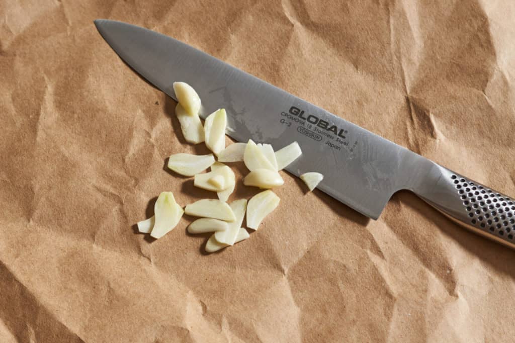 A chef's knife with sliced garlic.