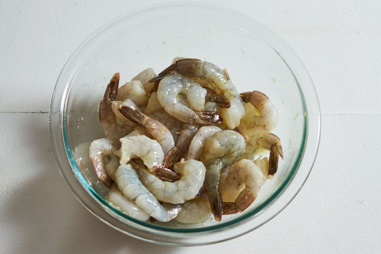 A glass bowl filled with raw shrimp marinating in olive oil and garlic.