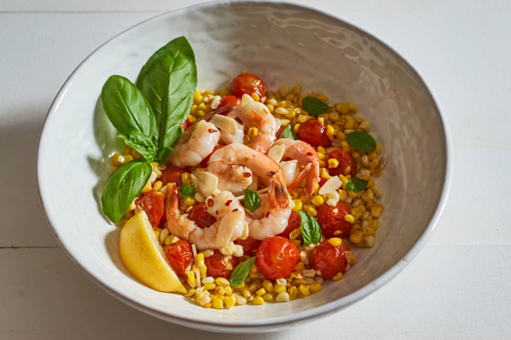 Shrimp scampi with tomatoes, corn, and fresh basil in a white serving bowl.