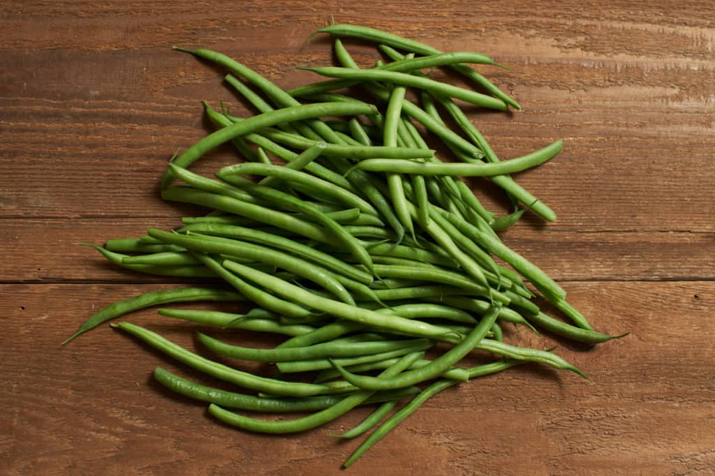 Fresh green beans (haricots verts) on a wooden surface.
