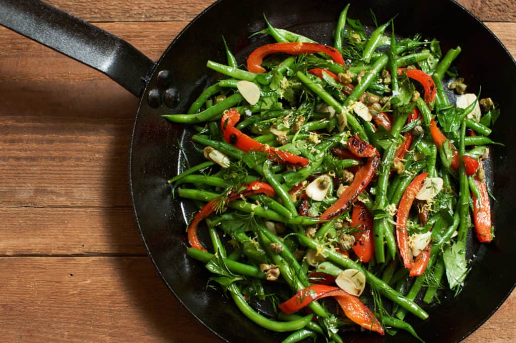 Fresh green bean salad with red peppers, capers and herbs in a cast iron skillet.