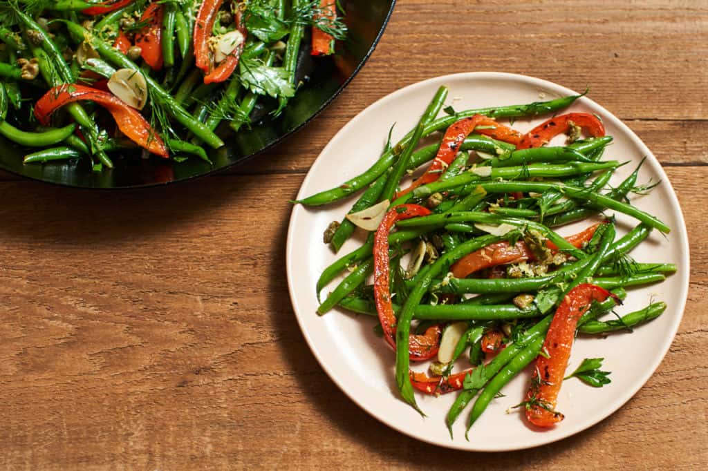 Fresh green bean salad with red peppers, capers and herbs on a plate.
