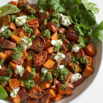 Oven roasted sweet potatoes with chile lime cilantro sauce in a white bowl.