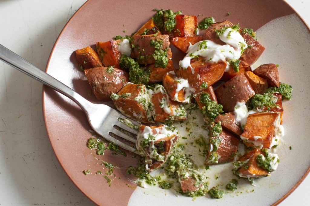 Oven roasted sweet potatoes with chile lime cilantro sauce on a brown and white plate.