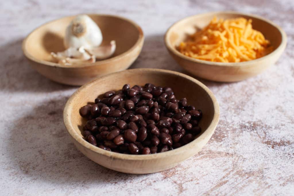 Black beans, cheddar cheese and garlic cloves in small wooden bowls.