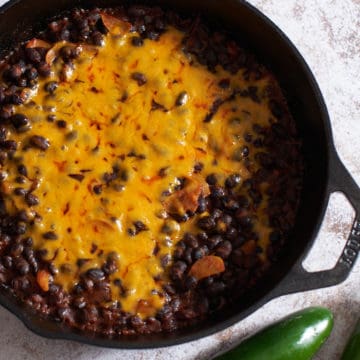 Spicy black beans with melted cheddar cheese in a cast iron skillet.