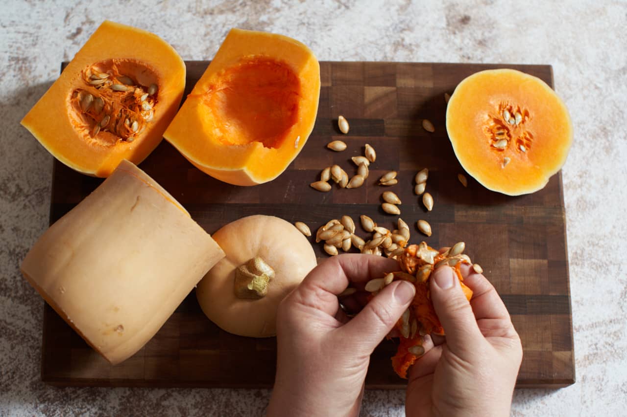 A woman's hands are shown separating butternut squash seeds from its pulp.