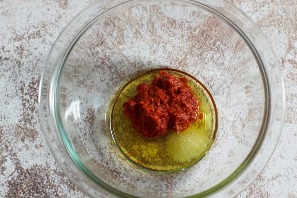 A glass bowl with harissa, olive oil and salt ready to be combined.