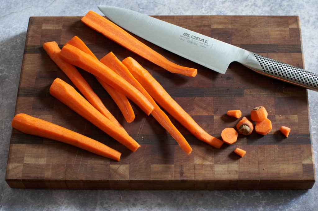 Peeled carrots on a cutting board with a chef's knife.