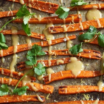 Oven roasted carrots with tahini sauce and cilantro on a baking sheet.