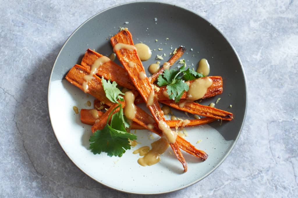 Oven roasted carrots with tahini sauce and cilantro on a gray and white plate.