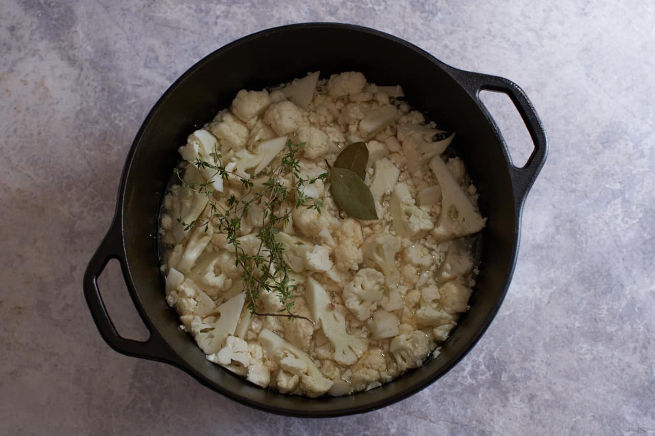 Chopped cauliflower in a pot with bay leaves and thyme.