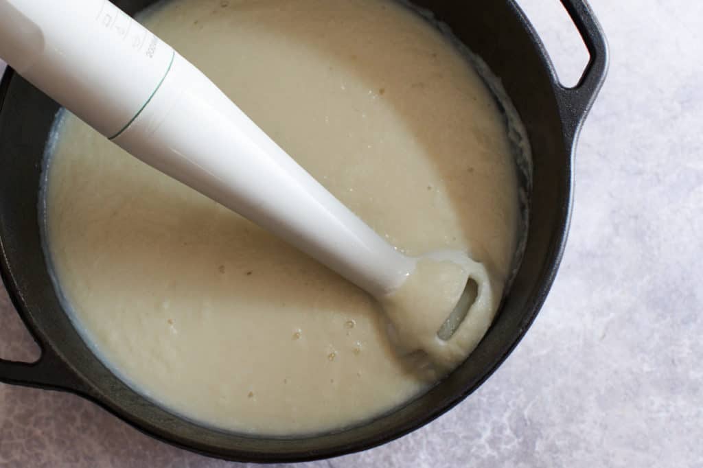 Creamy cauliflower soup in a pot with an immersion blender.