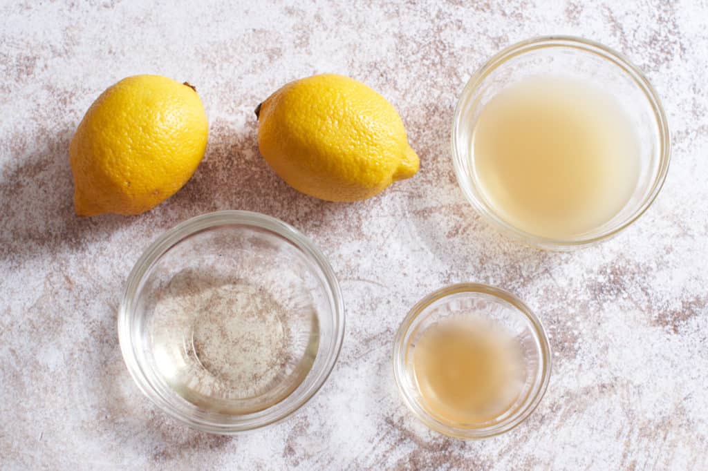 two lemons with three small glass bowls containing white wine, chicken stock and cider vinegar