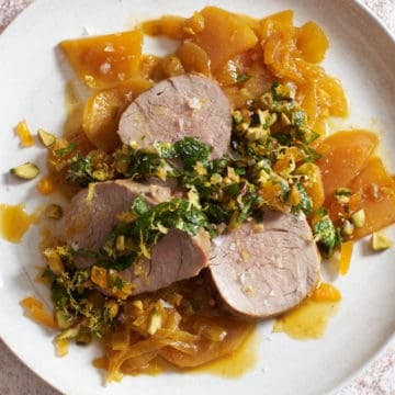 a plate of pork tenderloin with golden beets with a knife and fork and a dish of apricot mint sauce