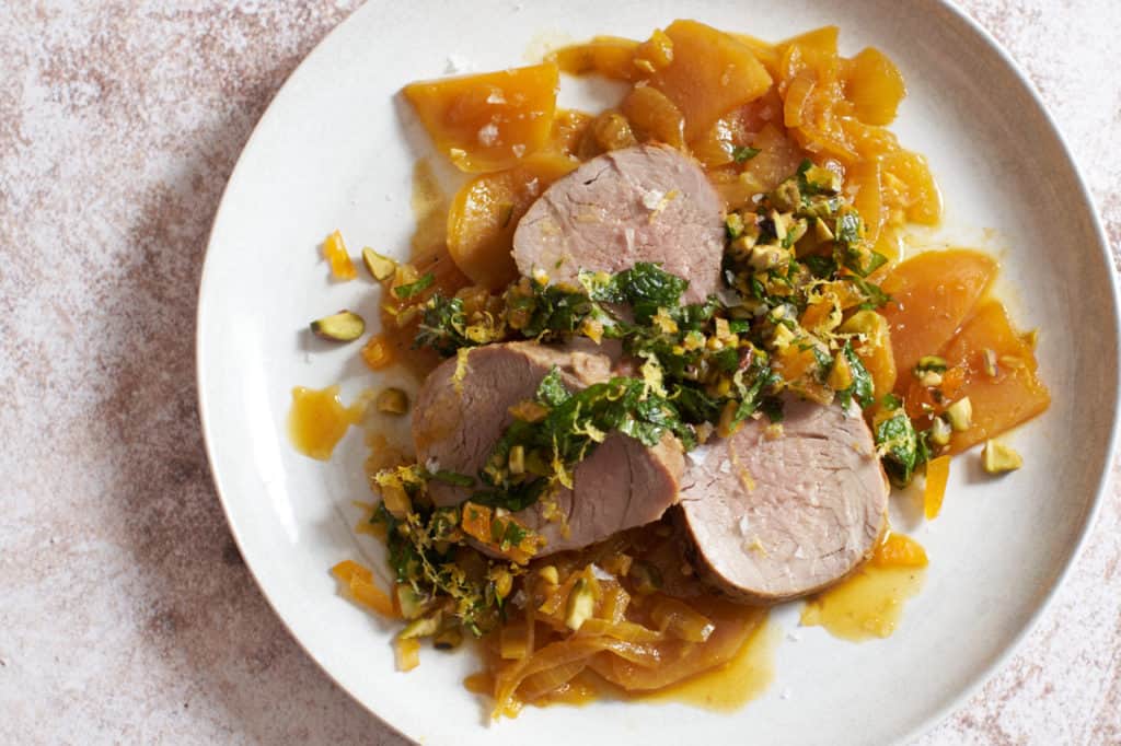 a plate of pork tenderloin with golden beets with a knife and fork and a dish of apricot mint sauce