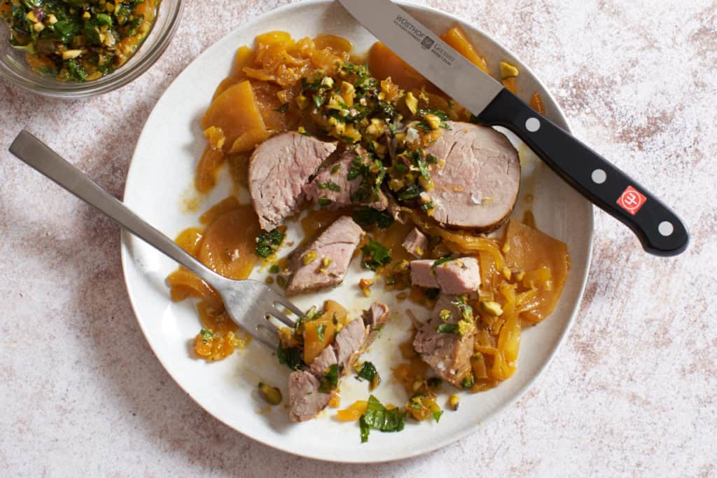 a plate of pork tenderloin with golden beets with a knife and fork and a dish of apricot mint sauce