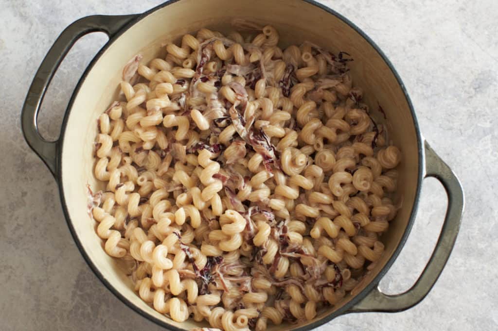 A dutch oven with cooked cavatappi coated in creamy goat cheese sauce