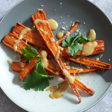 Oven roasted carrots with tahini sauce and cilantro on a gray and white plate.