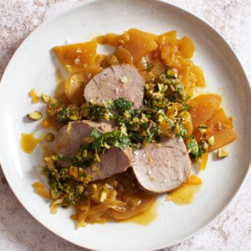 Sliced pork tenderloin atop golden beets and onions with an apricot-mint sauce on top on a white plate.