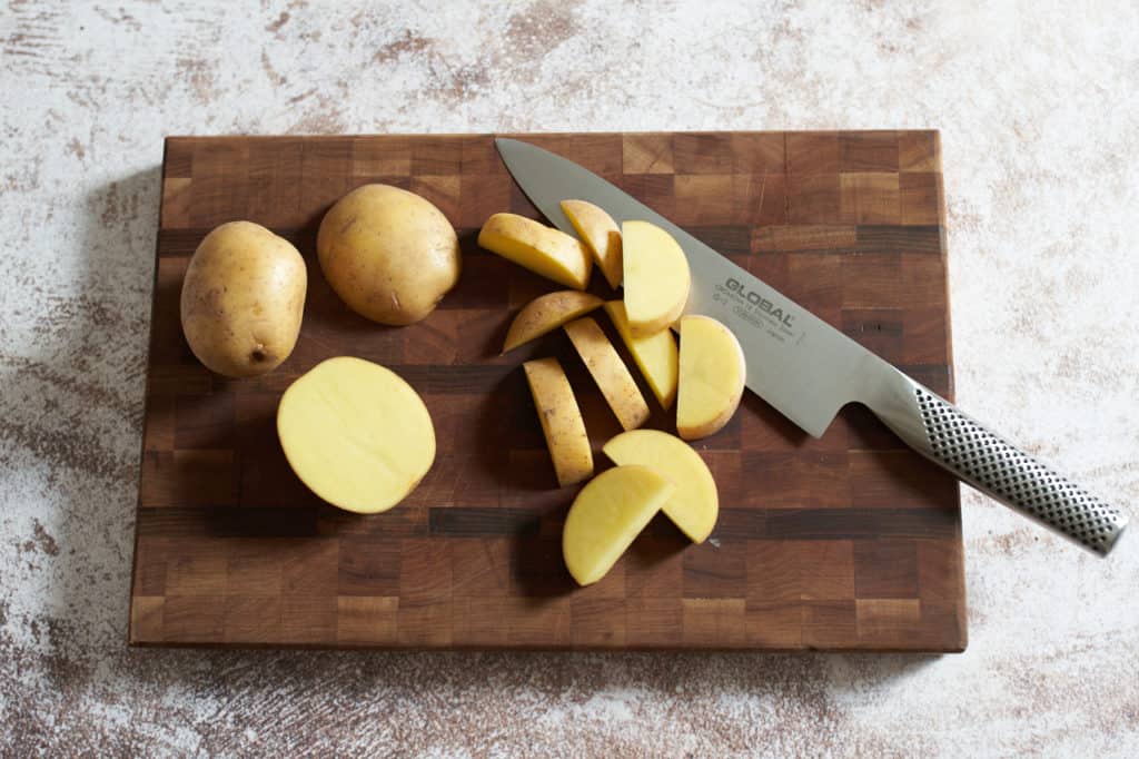 Sliced yukon gold potatoes on a cutting board with a knife.