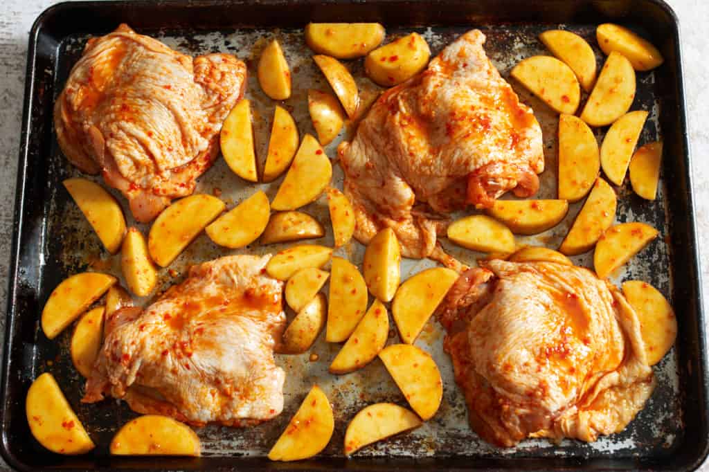Raw chicken and potatoes on a sheet pan.