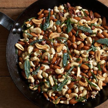 oven roasted nuts with rosemary, sage, and crispy garlic in a black skillet