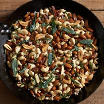oven roasted nuts with rosemary, sage, and crispy garlic in a black skillet