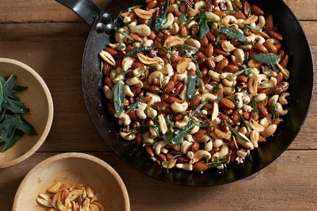 oven roasted nuts in a skillet next to two small wooden bowls with sage and garlic