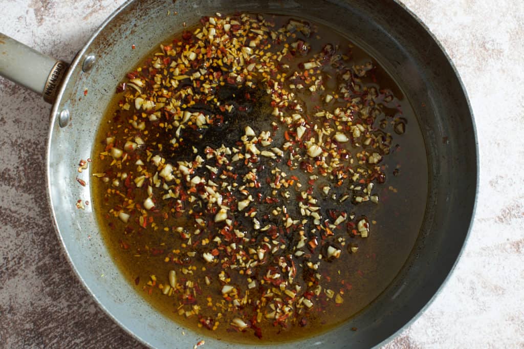 A skillet with chopped garlic, crushed red pepper and olive oil.
