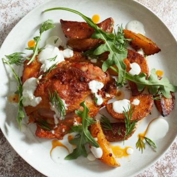 Harissa chicken thighs and potatoes on a white plate topped with herbs and yogurt sauce.