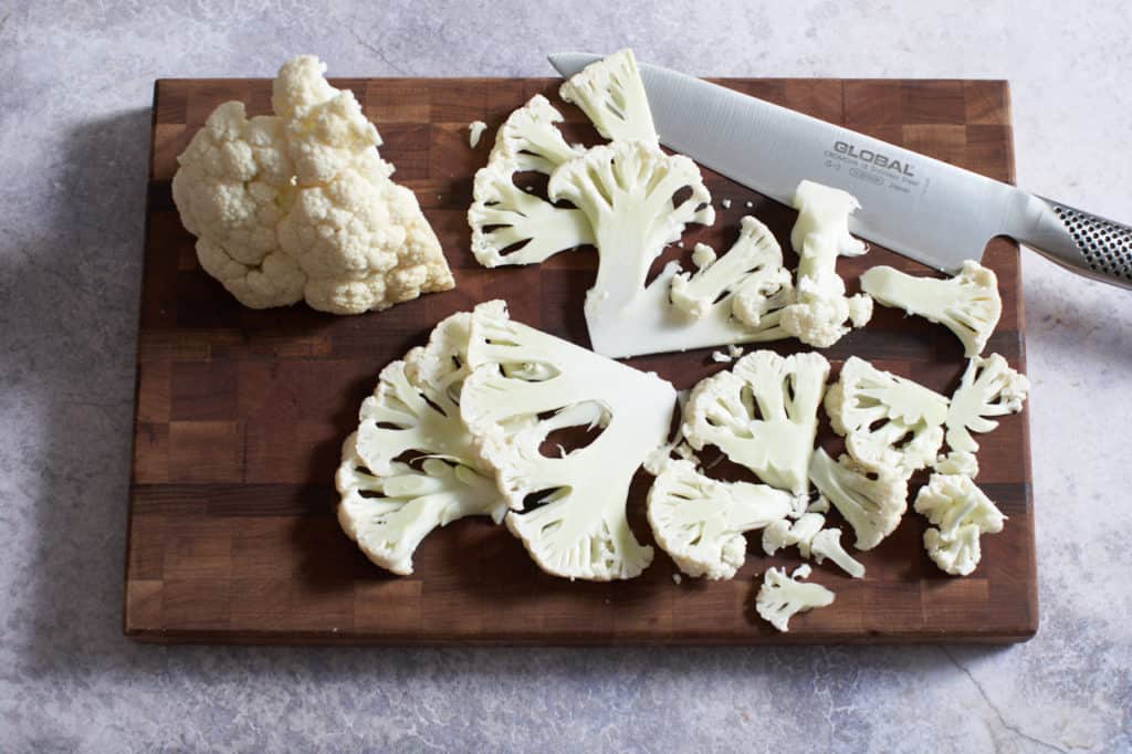 Sliced cauliflower and a chef's knife on a wooden cutting board.