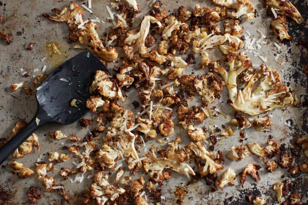 Crispy roasted cauliflower with parmesan and garlic on a sheet pan with a black spatula.