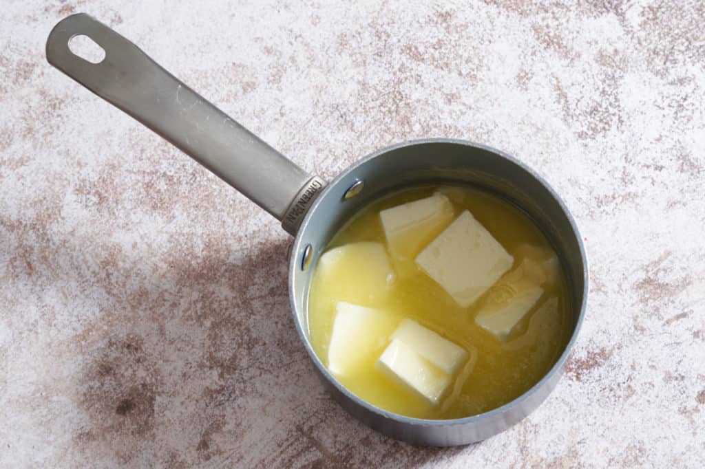 A sauce pan with melting pats of butter.