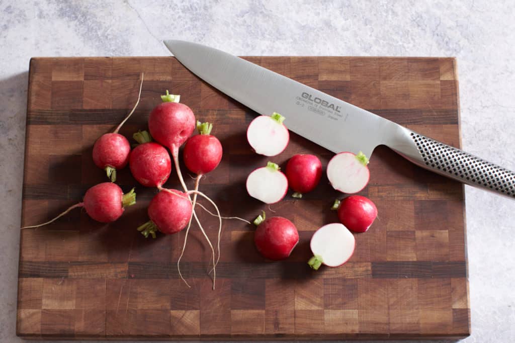 Radishes sliced in half and a chef's knife on a cutting board.