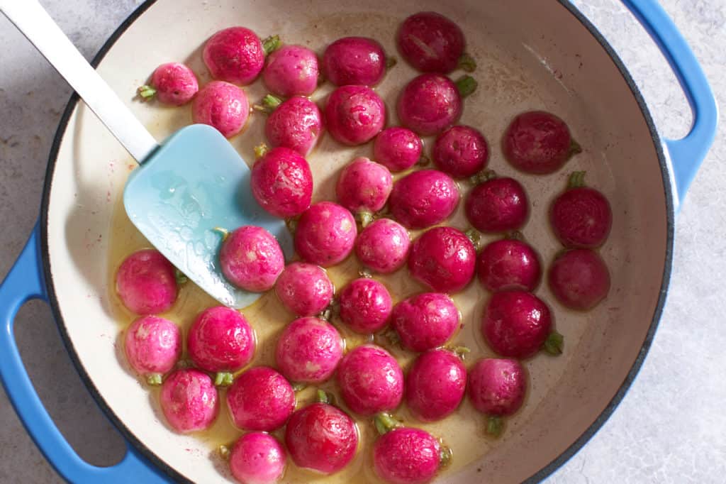 Cooked radish halves in an enamel pan with a spatula.