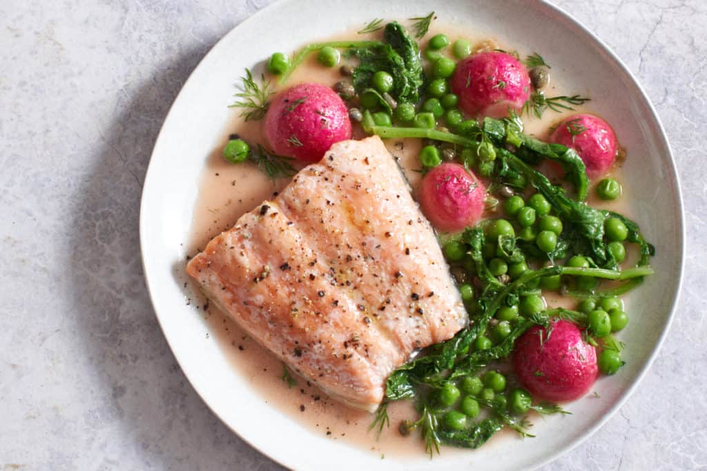 salmon with peas and radishes on a white plate.