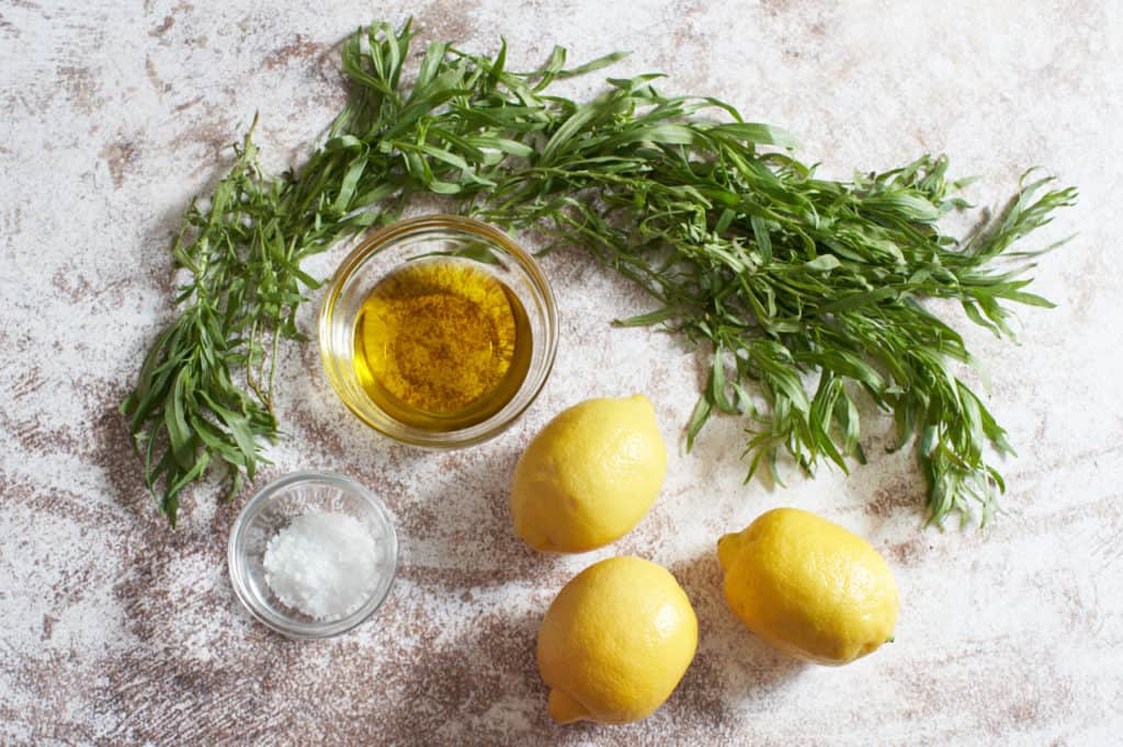 Fresh tarragon, three lemons and two small glass bowls with olive oil and sea salt. 