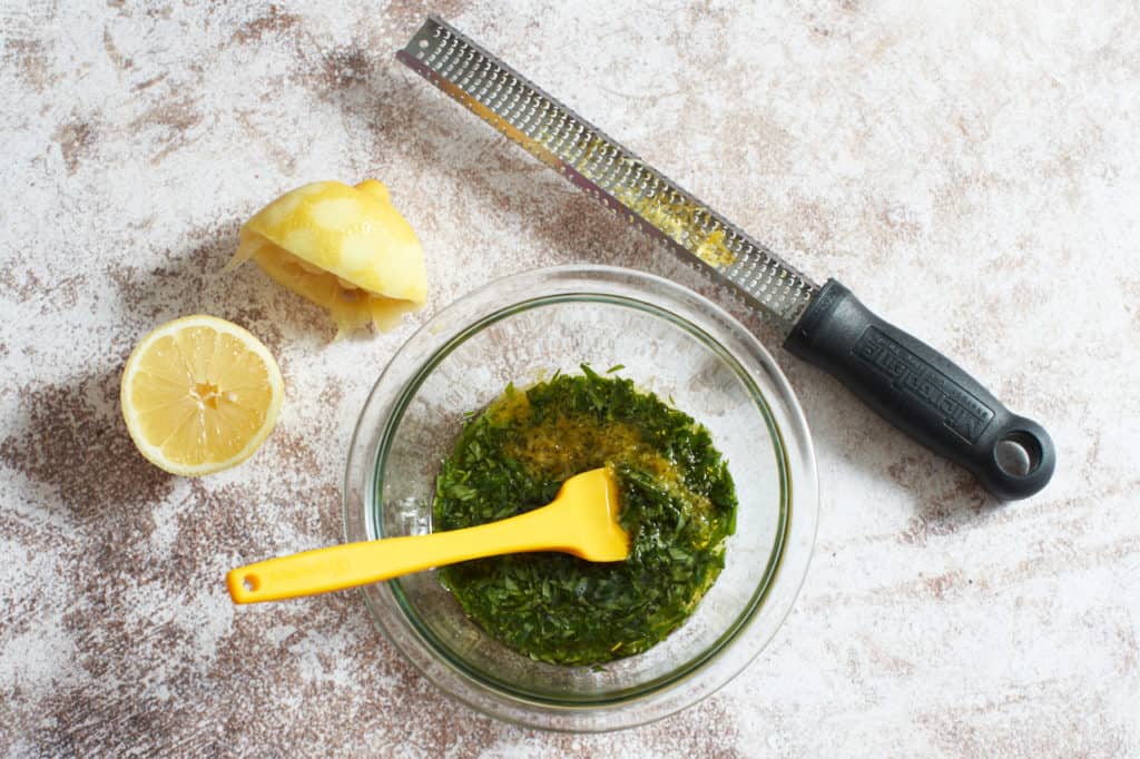 A bowl of olive oil, tarragon and lemon zest, a microplane grater, and two lemon halves.