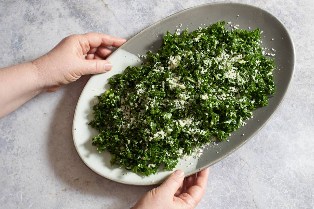 A woman's hands holding a gray and white platter of kale salad.