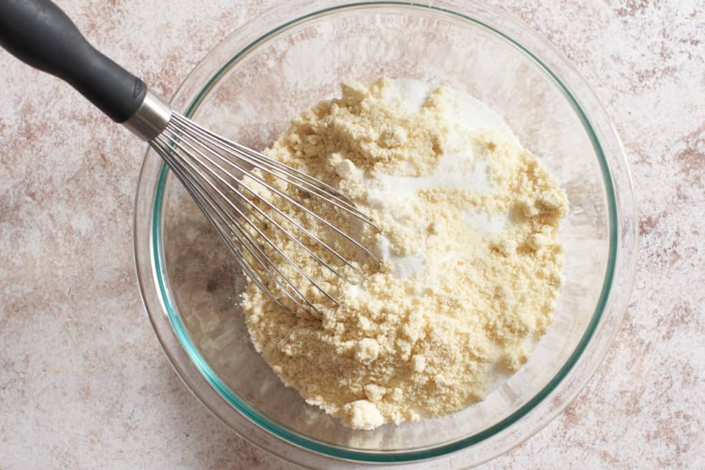 A bowl of dry almond flour and other dry ingredients with a whisk.