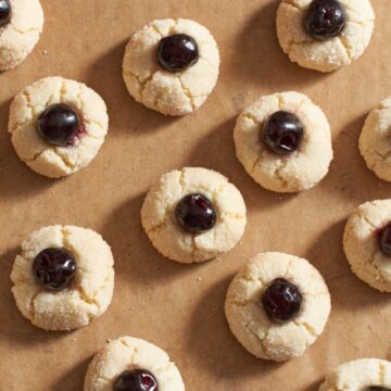 Amaretti cookies with a cherry on top of each one on brown parchment paper.