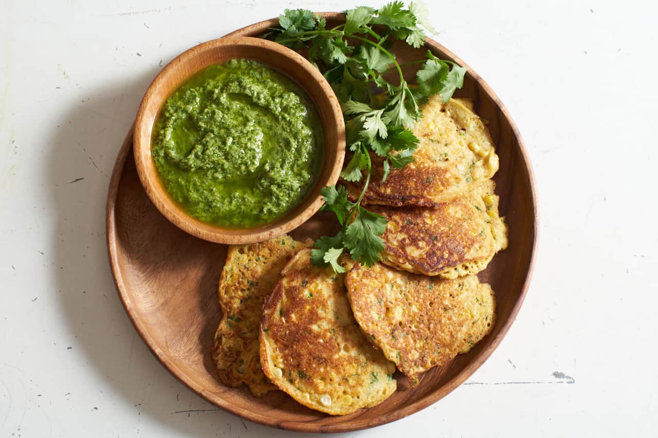 Corn cakes with a bowl of guasacaca on a wooden plate.