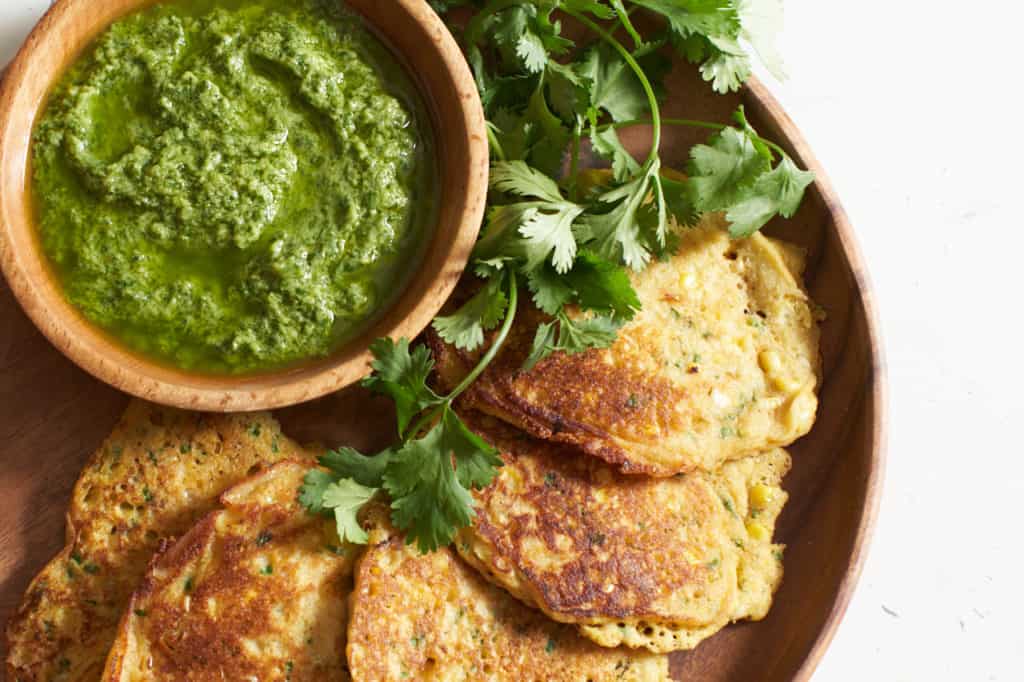 Corn cakes with a bowl of guasacaca on a wooden plate.