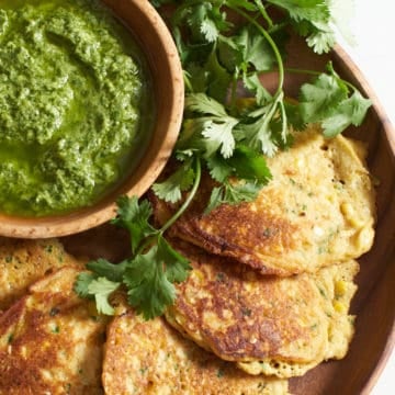 Corn cakes with a bowl of guasacaca on a wooden plate.