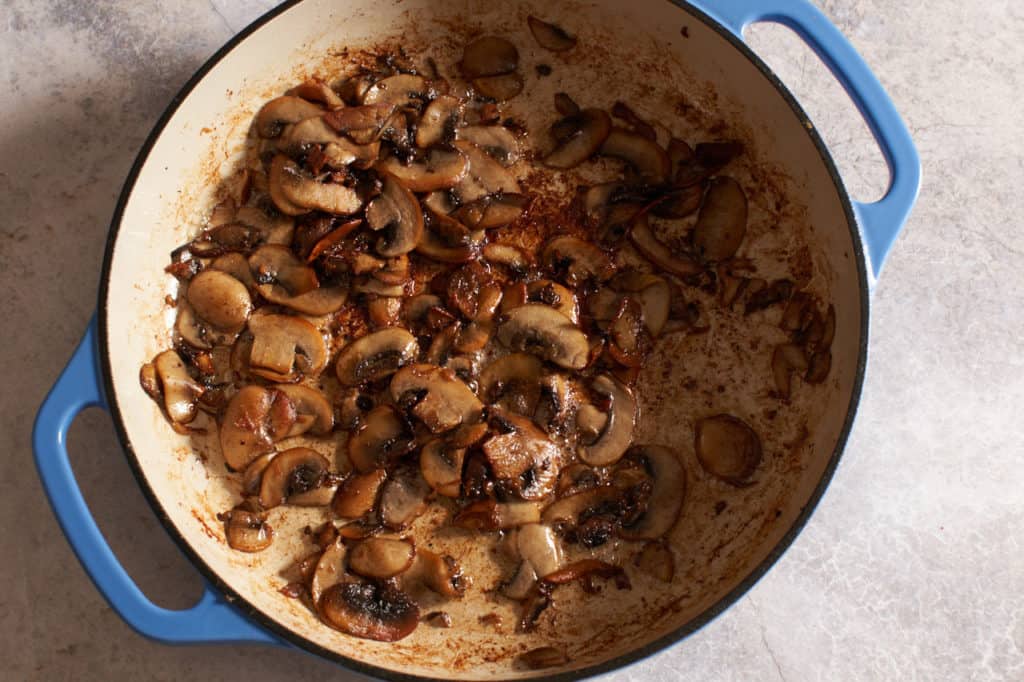 Browned mushrooms in a blue casserole pan.