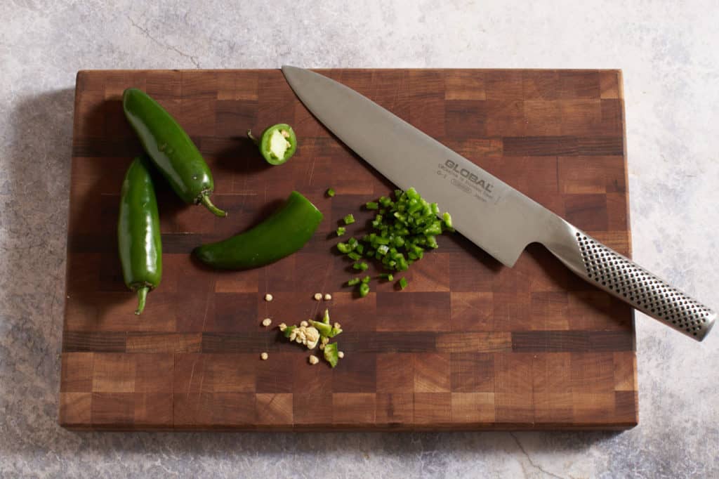 A knife on a cutting board with chopped and whole jalapeños.
