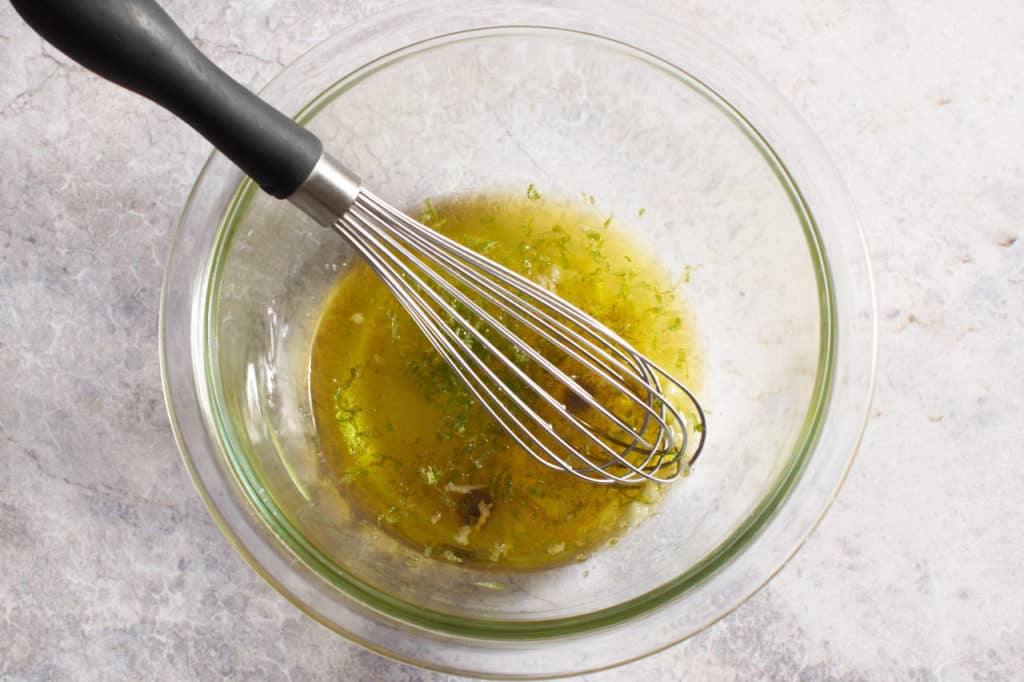 A whisk in a glass bowl with lime dressing.