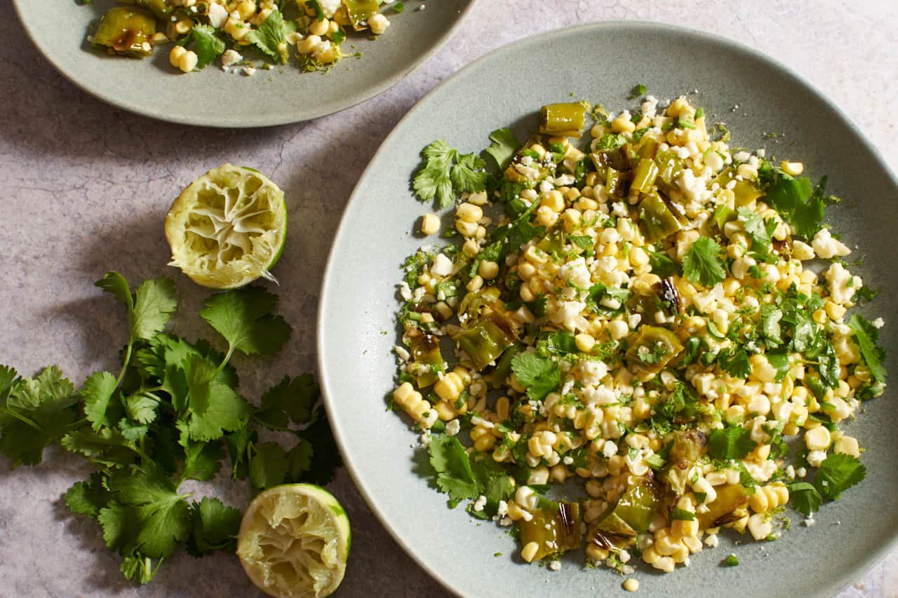 Fresh corn salad on gray plates next to cilantro and squeezed limes.