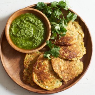 Corn cakes on a platter arranged in a half circle around a bowl of guasacaca sauce, garnished with fresh cilantro.